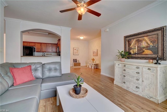 living area featuring arched walkways, a ceiling fan, crown molding, and light wood-style floors