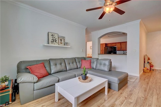 living room with ornamental molding, arched walkways, light wood finished floors, baseboards, and ceiling fan