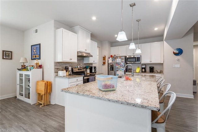 kitchen featuring backsplash, under cabinet range hood, a kitchen bar, appliances with stainless steel finishes, and white cabinetry