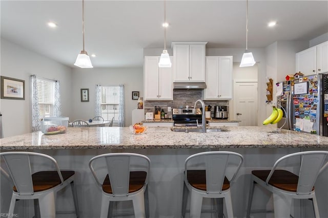 kitchen featuring tasteful backsplash, under cabinet range hood, stainless steel range with electric cooktop, white cabinets, and a sink