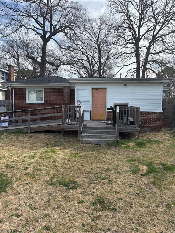 rear view of house featuring a yard, brick siding, a deck, and fence