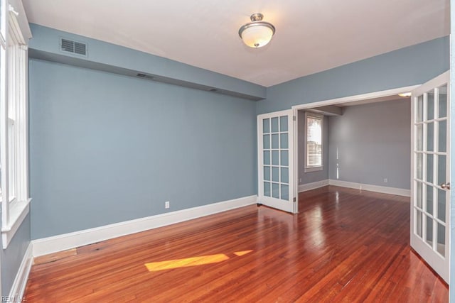 empty room featuring wood finished floors, french doors, visible vents, and baseboards