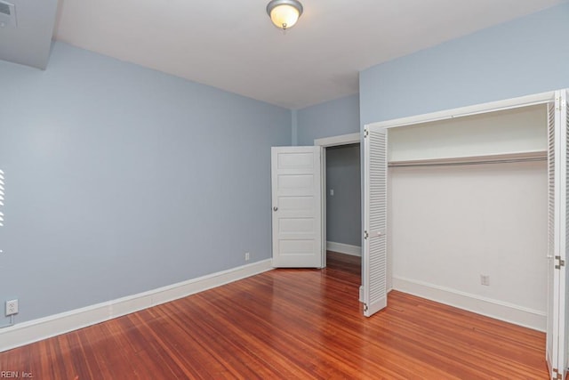 unfurnished bedroom with visible vents, wood finished floors, a closet, and baseboards