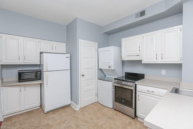 kitchen featuring electric range, visible vents, stacked washing maching and dryer, freestanding refrigerator, and black microwave