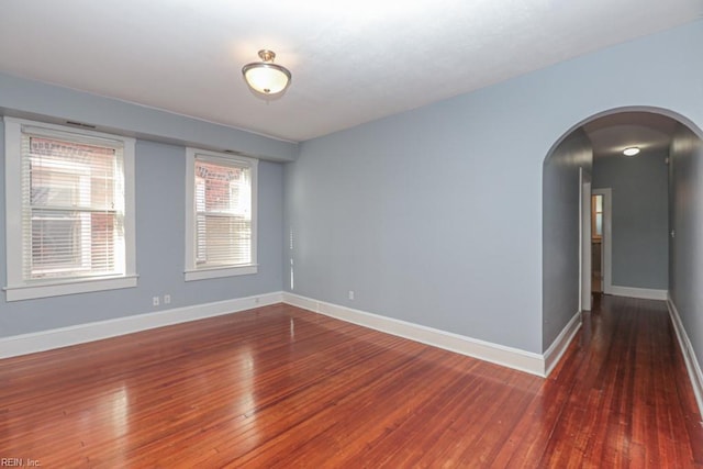 unfurnished room featuring baseboards, arched walkways, and hardwood / wood-style flooring