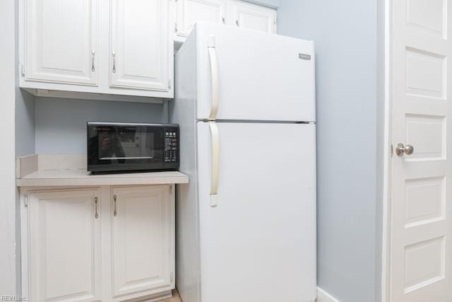 kitchen featuring white cabinetry, light countertops, black microwave, and freestanding refrigerator