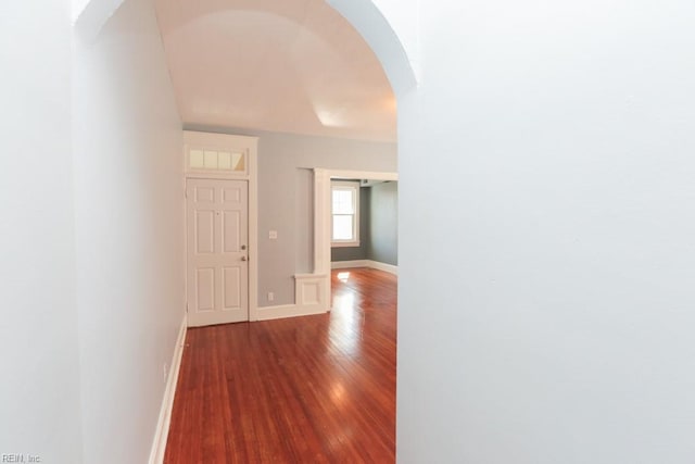 hallway featuring baseboards, arched walkways, and wood finished floors