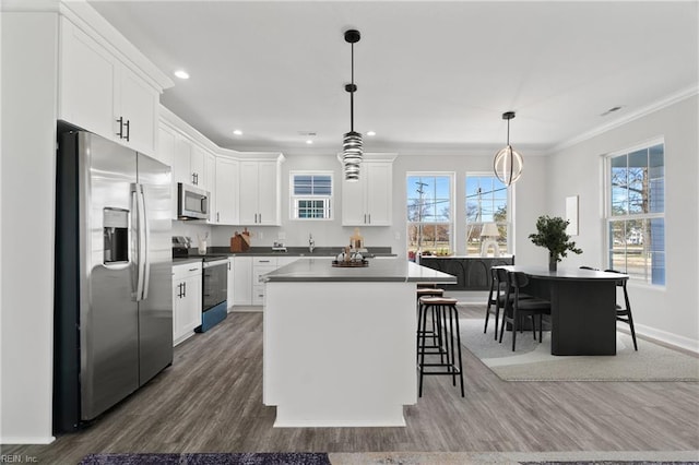 kitchen with stainless steel appliances, wood finished floors, white cabinets, and crown molding