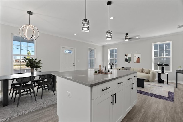 kitchen featuring a center island, crown molding, open floor plan, light wood-style floors, and white cabinets