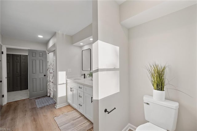 bathroom with toilet, wood finished floors, recessed lighting, baseboards, and vanity