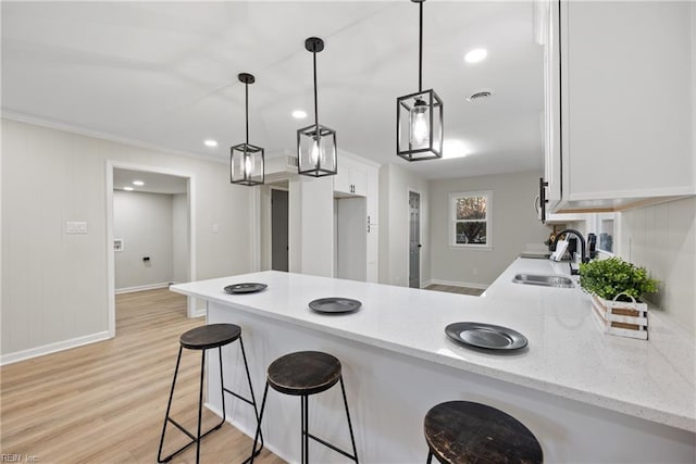 kitchen with visible vents, a sink, white cabinetry, light wood-style floors, and a peninsula