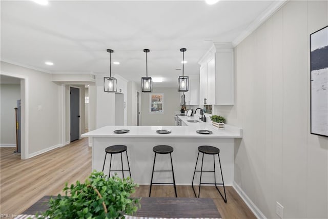 kitchen with a sink, a peninsula, white cabinets, light wood finished floors, and light countertops