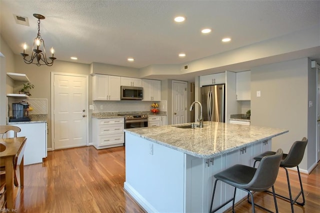 kitchen featuring visible vents, a sink, wood finished floors, stainless steel appliances, and white cabinets