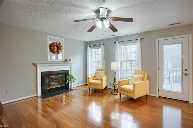 sitting room featuring wood finished floors, visible vents, ceiling fan, a textured ceiling, and a glass covered fireplace