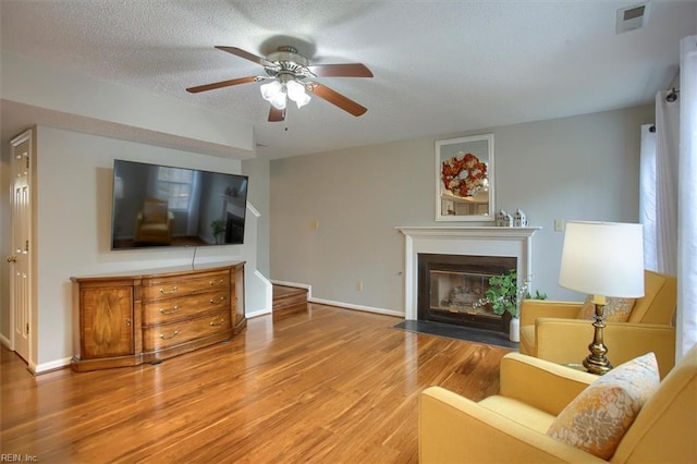 living area featuring wood finished floors, visible vents, a fireplace with flush hearth, ceiling fan, and a textured ceiling