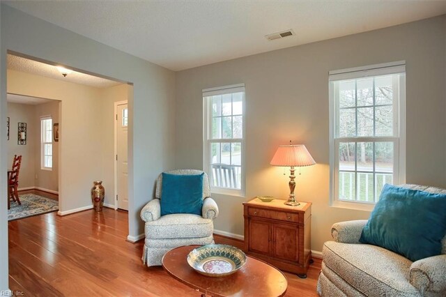 living area featuring a wealth of natural light, visible vents, and wood finished floors