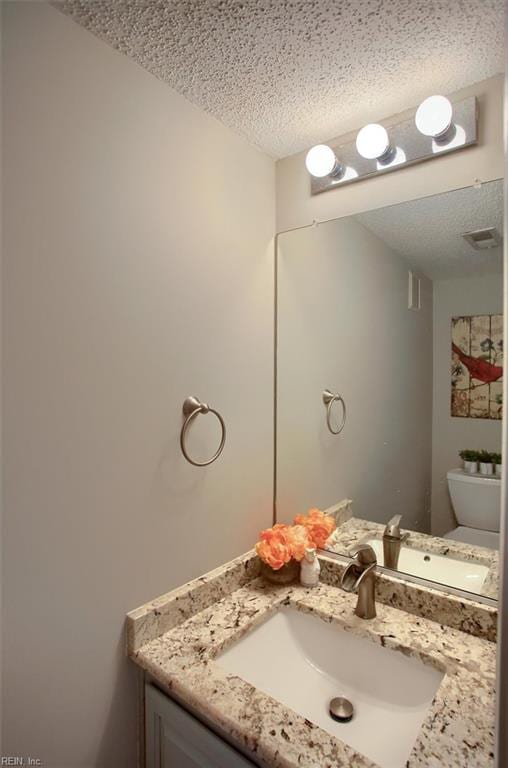 half bath featuring visible vents, a textured ceiling, vanity, and toilet