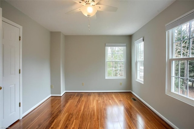 empty room featuring a ceiling fan, visible vents, wood finished floors, and baseboards