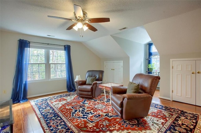 living area with a wealth of natural light, visible vents, a ceiling fan, and vaulted ceiling