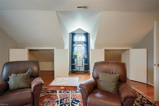 living area with visible vents, lofted ceiling, a textured ceiling, and wood finished floors