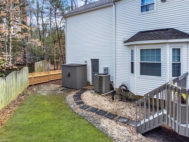 exterior space featuring cooling unit, roof with shingles, a yard, and fence