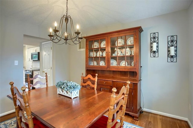 dining area with a chandelier, a textured ceiling, baseboards, and wood finished floors