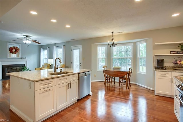 kitchen featuring light wood-type flooring, ceiling fan with notable chandelier, stainless steel dishwasher, white cabinets, and a sink