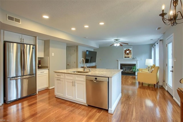 kitchen featuring light wood-type flooring, ceiling fan with notable chandelier, a glass covered fireplace, stainless steel appliances, and a sink