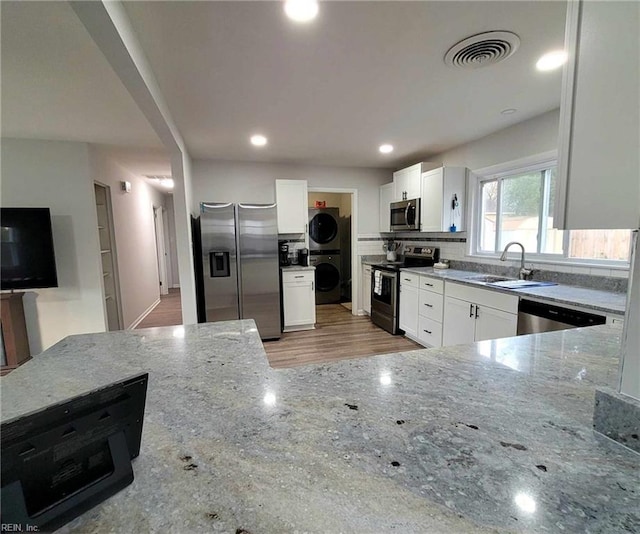 kitchen with light stone counters, visible vents, stacked washing maching and dryer, a sink, and stainless steel appliances