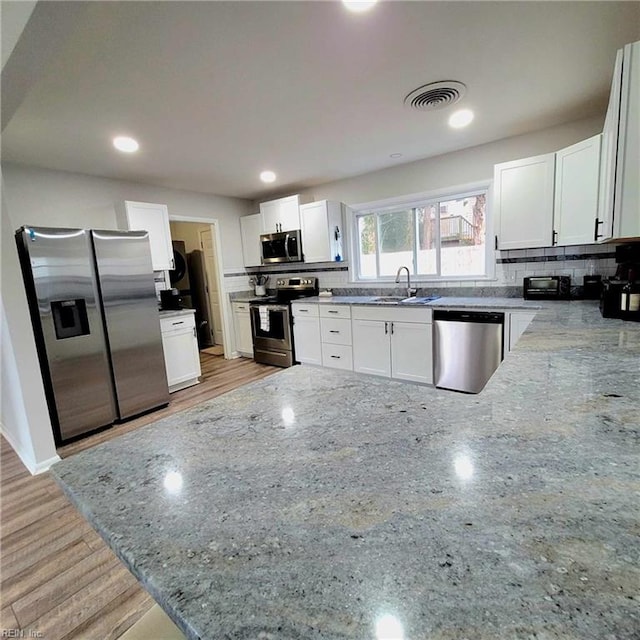 kitchen with light stone counters, visible vents, a peninsula, decorative backsplash, and appliances with stainless steel finishes