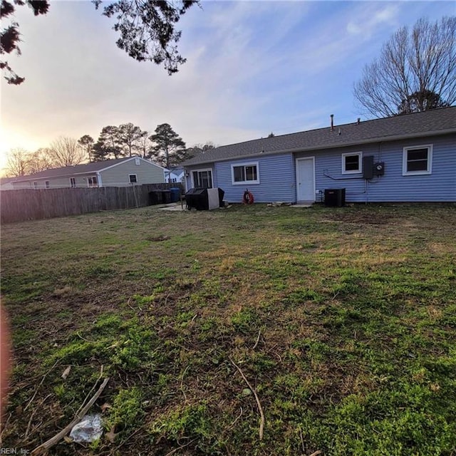 back of property at dusk featuring central air condition unit, a lawn, and fence