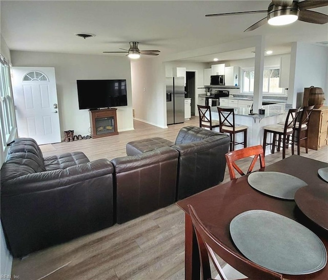 living area with baseboards, a fireplace, a ceiling fan, and light wood-style floors