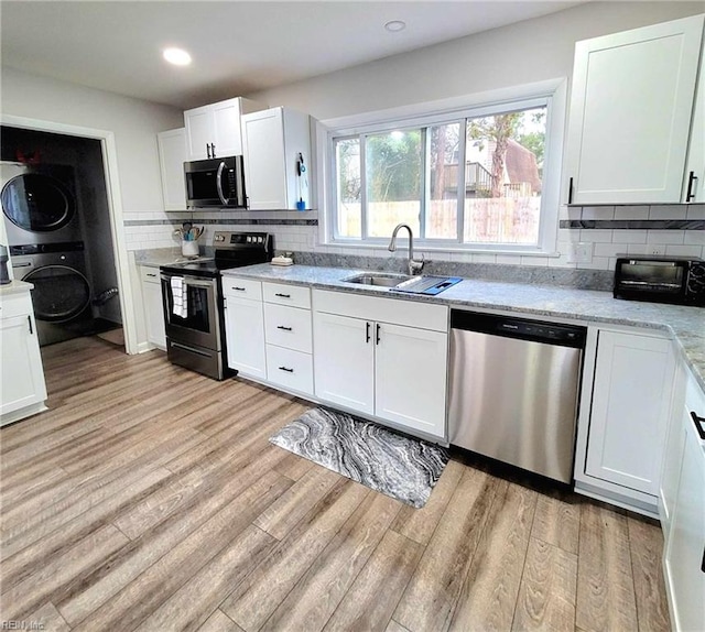 kitchen featuring a toaster, stacked washer and dryer, light wood-style flooring, stainless steel appliances, and a sink