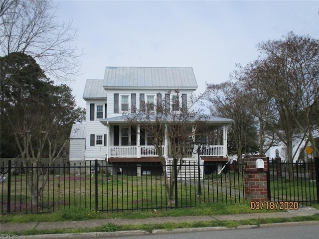 view of front of home with metal roof, covered porch, a fenced front yard, and a front lawn