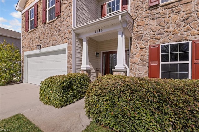 property entrance with stone siding, driveway, and a garage