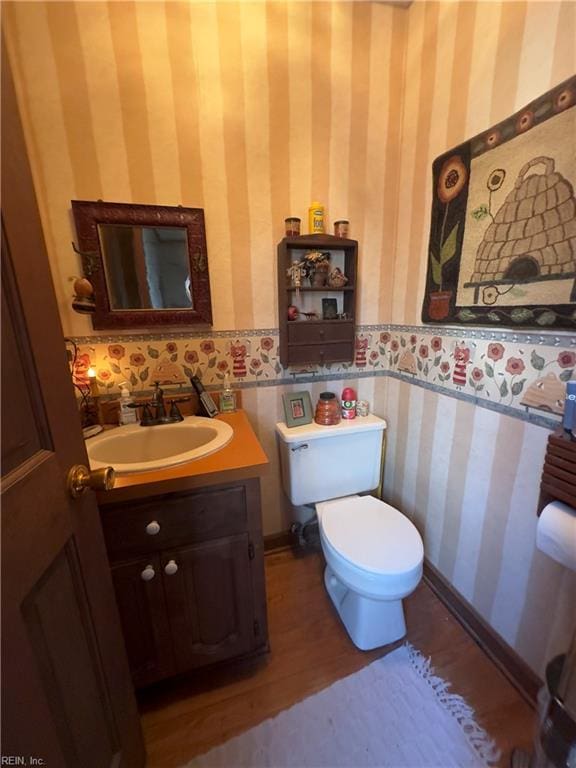 half bathroom with toilet, wallpapered walls, vanity, and baseboards