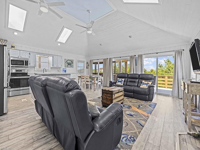 living room with lofted ceiling with skylight, recessed lighting, light wood-style flooring, and a ceiling fan