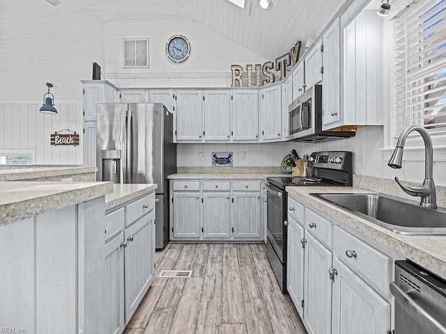 kitchen with light wood finished floors, light countertops, vaulted ceiling, appliances with stainless steel finishes, and a sink