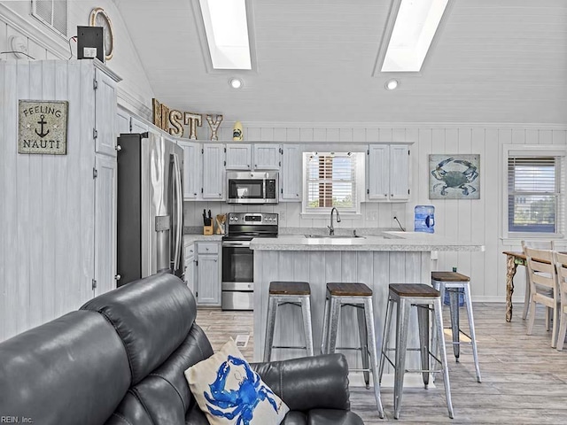 kitchen featuring a breakfast bar area, a sink, light countertops, appliances with stainless steel finishes, and lofted ceiling with skylight