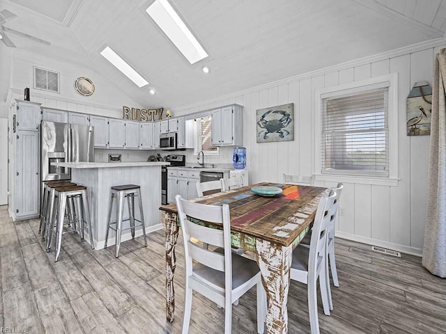 dining area featuring vaulted ceiling with skylight, light wood-style flooring, and visible vents