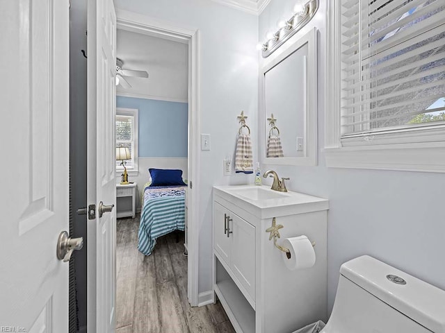 half bathroom with wood finished floors, toilet, ornamental molding, and vanity