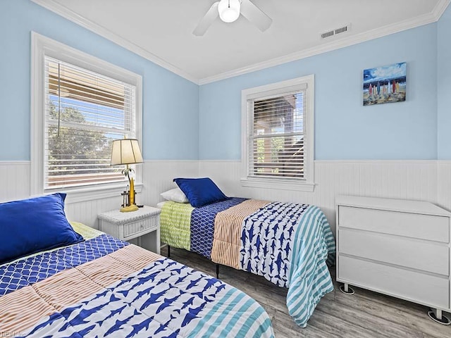 bedroom featuring visible vents, ornamental molding, wood finished floors, wainscoting, and ceiling fan