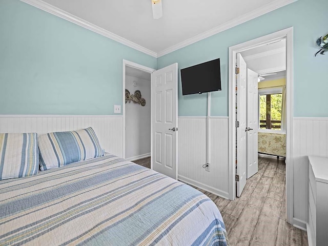 bedroom featuring light wood finished floors, a wainscoted wall, crown molding, and a ceiling fan