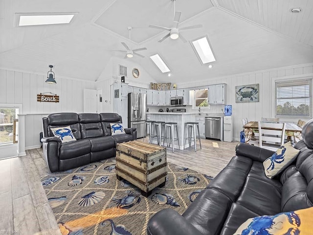 living room featuring a wealth of natural light, vaulted ceiling with skylight, a ceiling fan, and light wood finished floors