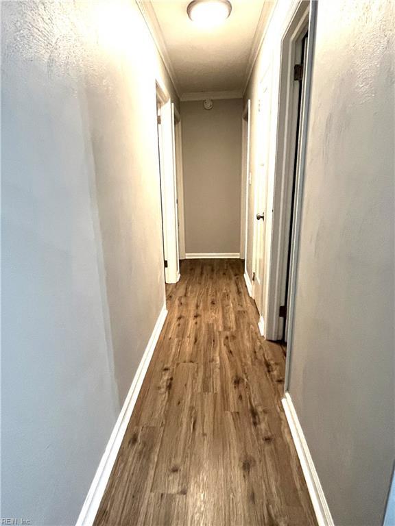 corridor featuring baseboards, wood finished floors, and crown molding