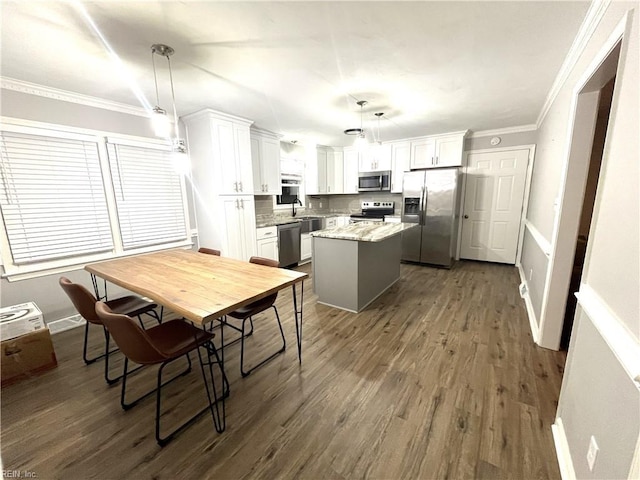 kitchen with ornamental molding, dark wood-type flooring, appliances with stainless steel finishes, white cabinetry, and a center island