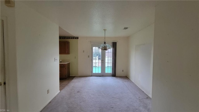 unfurnished dining area with visible vents, french doors, a textured ceiling, light carpet, and a notable chandelier