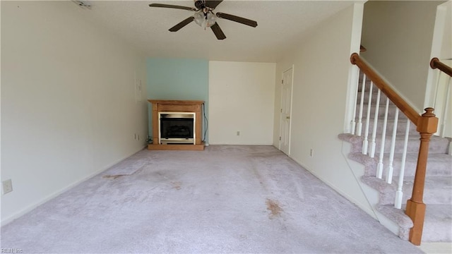 unfurnished living room with stairs, carpet floors, a ceiling fan, and a fireplace