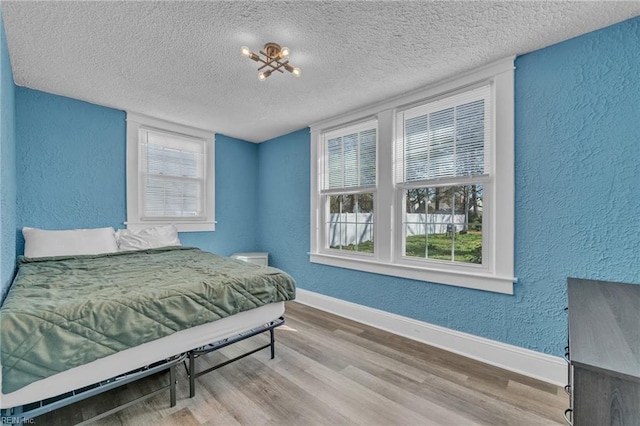 bedroom featuring baseboards, a textured ceiling, wood finished floors, and a textured wall