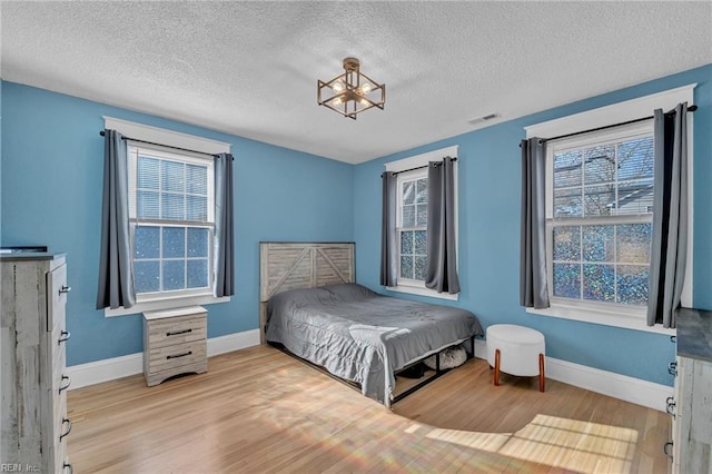 bedroom featuring a textured ceiling, wood finished floors, visible vents, and baseboards